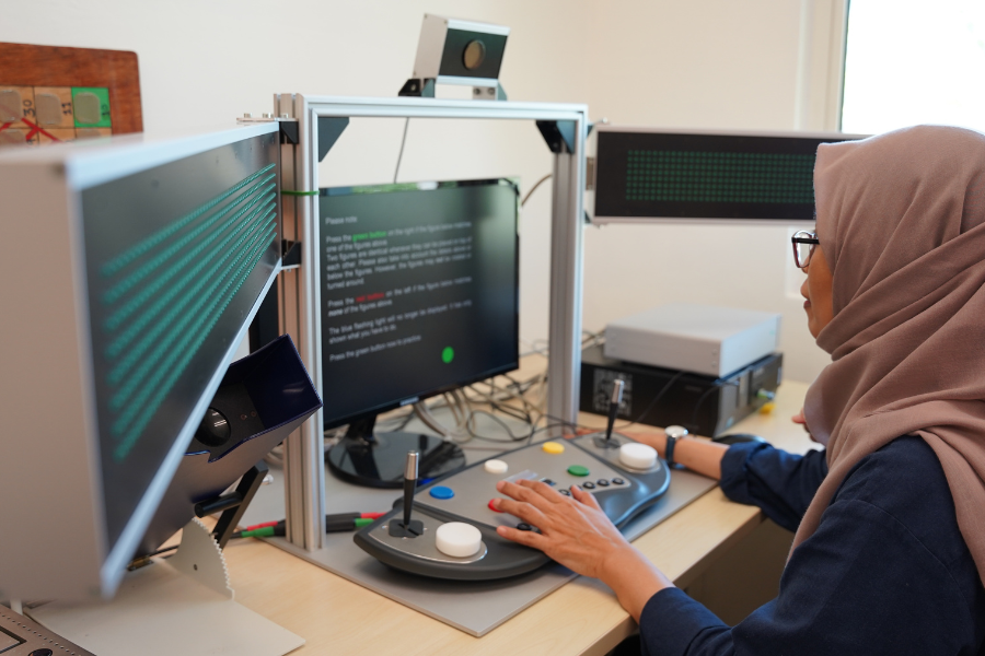 Woman using a cognitive assessment device with buttons, joysticks, and light panels.